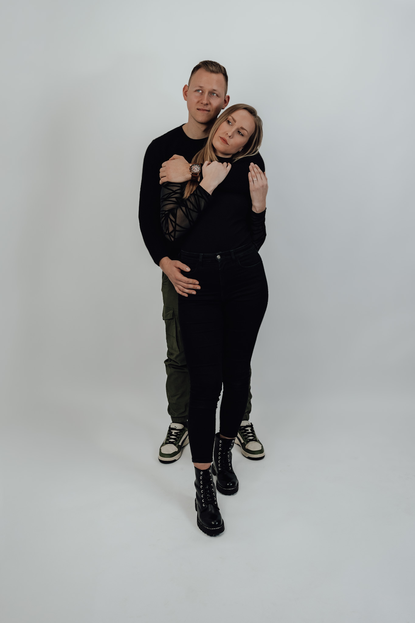 Ein Paar steht eng umschlungen vor hellem Hintergrund und schaut ruhig in die Ferne.